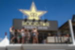 Meshbanner - ideal für Außenwerbung mit Windlast Banner Netzvinyl mit Rockstar Energy Drink Logo an Eventstand mit Terrasse bei sonnigem Wetter, Personen davor