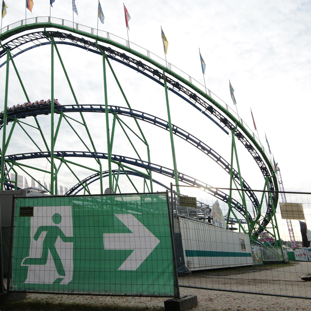 Notausgangsbanner mit Pfeil nach rechts am Bauzaun vor Achterbahnkonstruktion auf einem Volksfestgelände