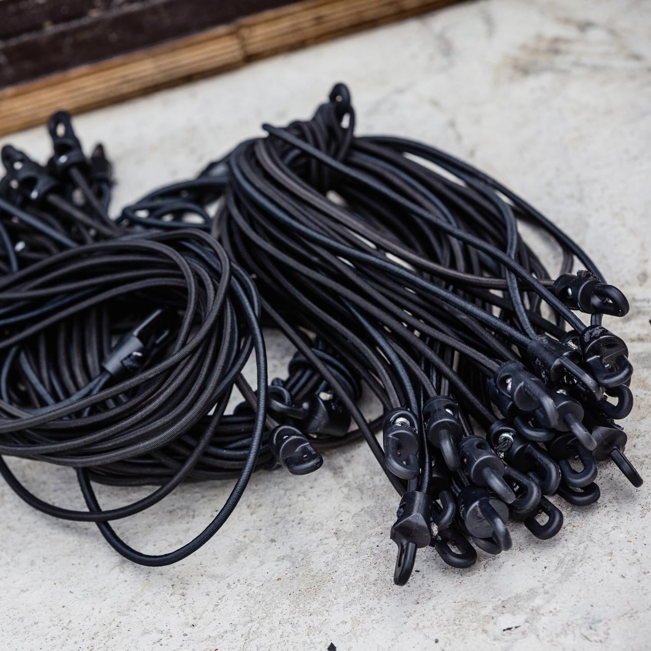 Draufsicht mehrerer schwarzer Spannfixe mit Haken, lose nebeneinander auf hellem Untergrund abgelegt
