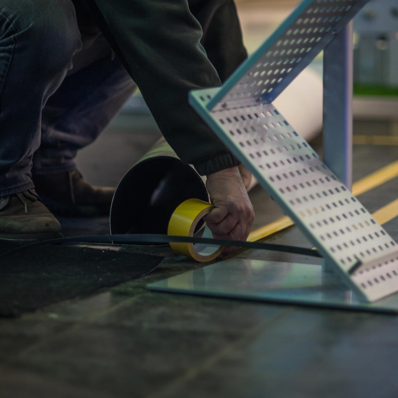 Detailaufnahme einer hockenden Person, die GT 703 mit gelber Abdeckung zur Fixierung eines Bodenbelages aufklebt