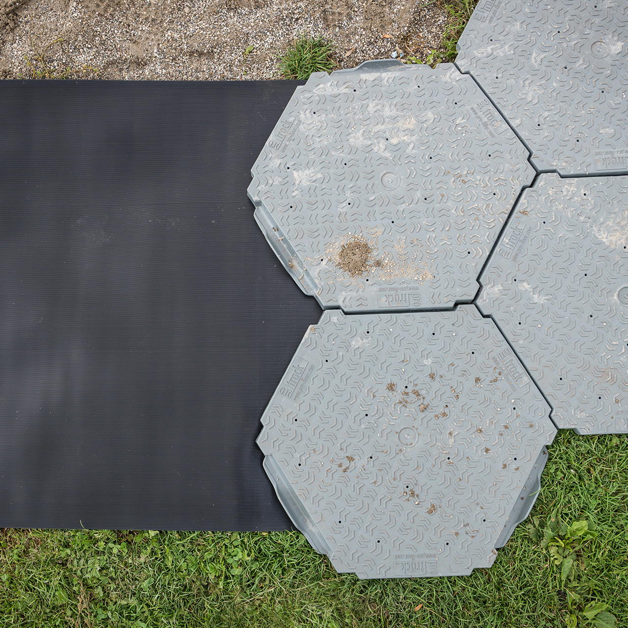 Strapazierfähiger Gummiläufer auf Gras und Kies angrenzend an hexagonale Bodenplatten im Outdoorbereich verlegt