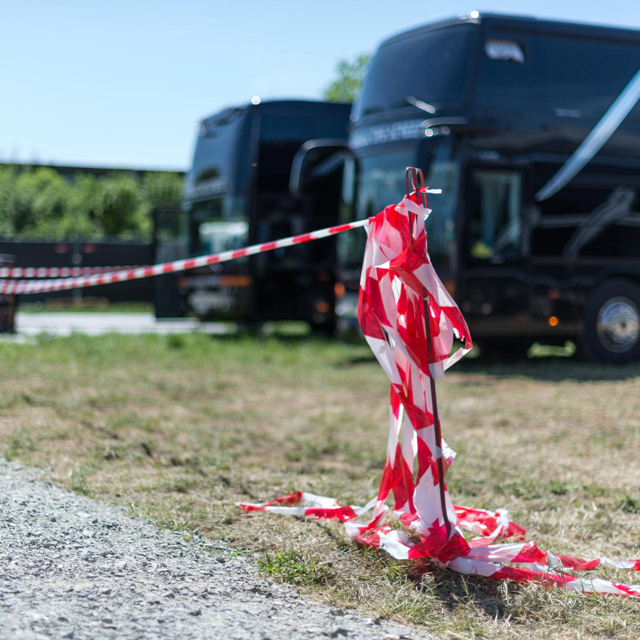 An einem Absperrstab befestigtes rot-weißes Trassierband zur temporären Abgrenzung eines Parkbereichs mit Tourbussen