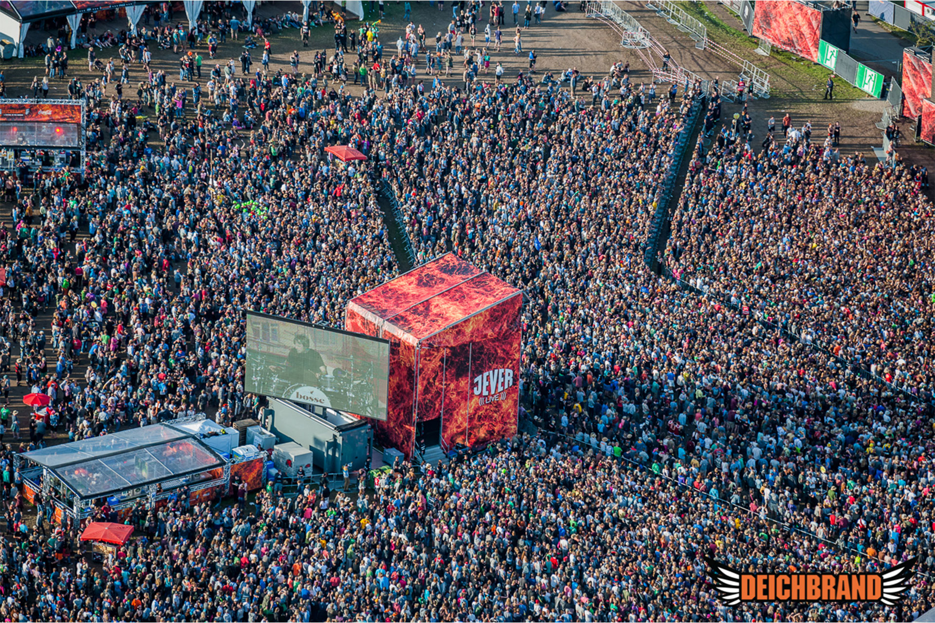 FOH-Turm auf Festivalwiese, vollflächig verkleidet mit rot-orange bedrucktem Frontlit PVC Banner mit weißem Schriftzug 