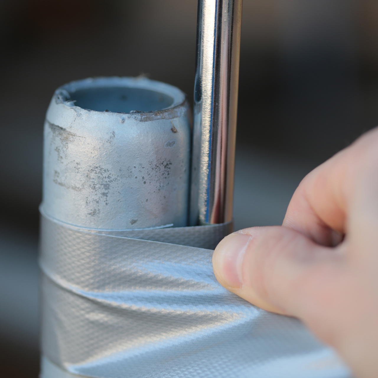 Eine Hand wickelt zur Fixierung silbernes Gewebeklebeband in mehreren Lagen um zwei Metallstangen 