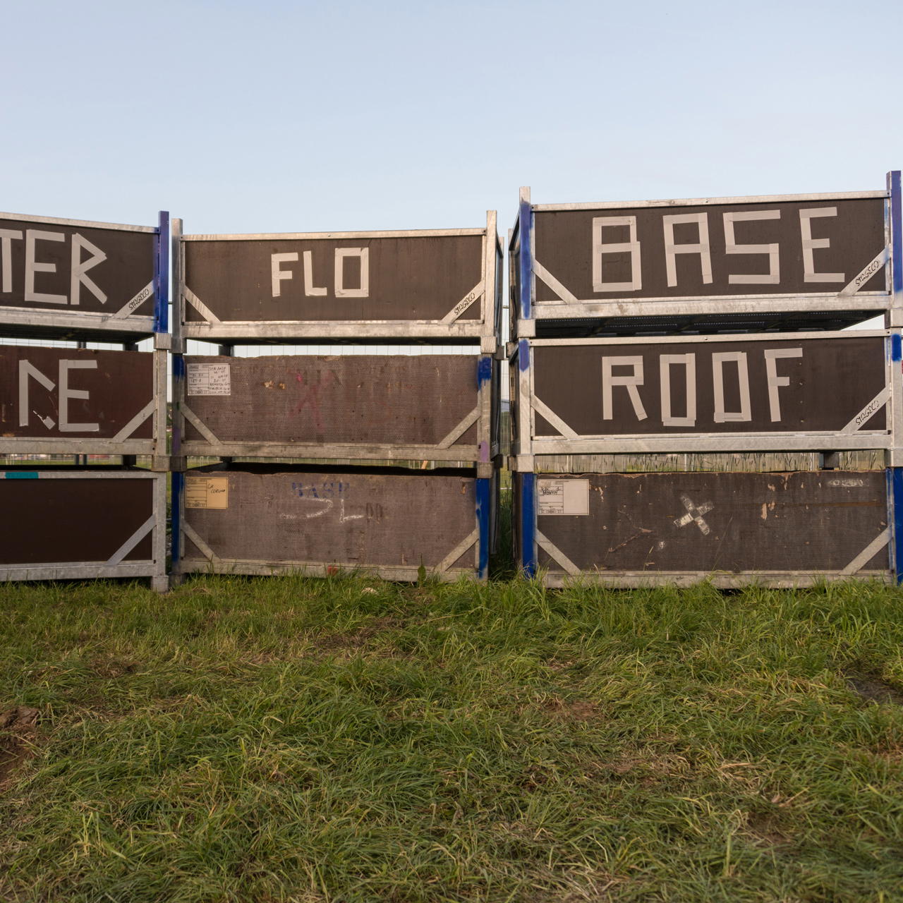 Mehrere gestapelte Bühnenteile auf einer Wiese mit teilweise großen Markierungen aus weißem Gaffa Tape