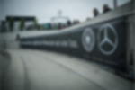 Meshbanner - Werbebanner hochauflösend und vollflächig bedruckt Geöstes Netzvinylbanner bedruckt mit Sponsorenbranding von Mercedes-Benz und DFB entlang eines Zauns mit Zuschauern