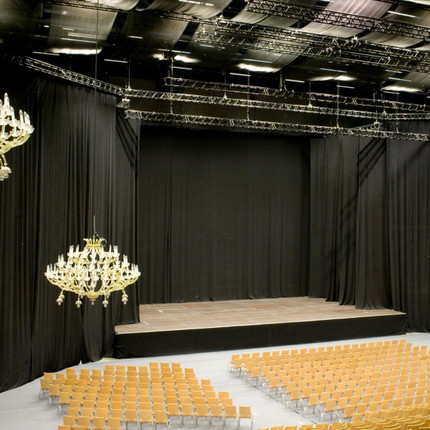 Moltonstoff schwarz nach individuellem Mass konfektionert Schwarzer Moltonstoff als Bühnenvorhang auf einer Bühne, davor Sitzplätze und Chandelier-Beleuchtung
