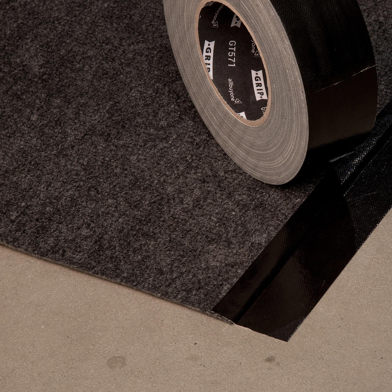 Teils verklebte Ecke eines grau-melierten Rips Teppichs, darauf eine schräg stehende Klebebandrolle