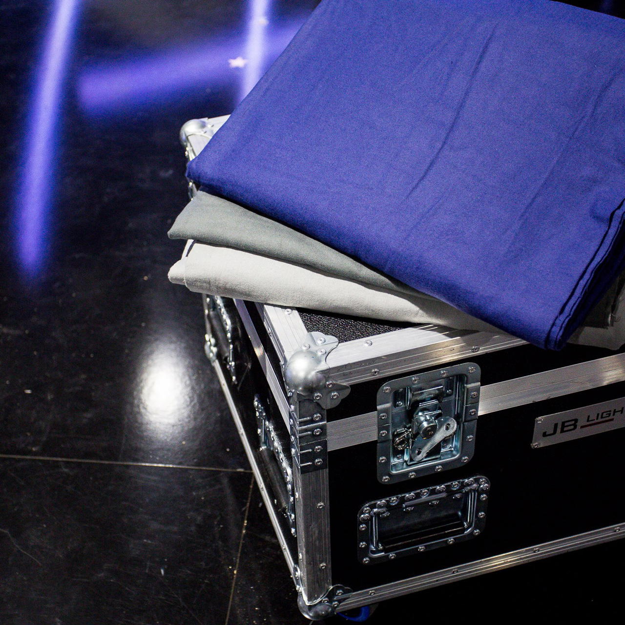 Gefaltete Molton Stoffe in Blau, Grau und Weiß liegen fächerförmig auf einem am Boden liegenden schwarzen Technikkoffer