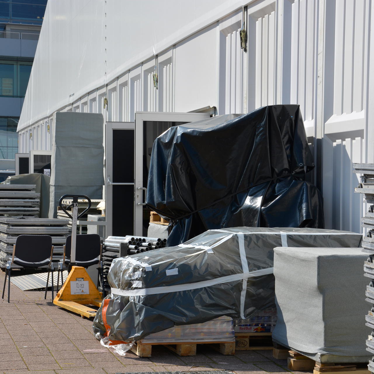 Weißes Gewebeklebeband fixiert eine transparente Abdeckfolie mit Transportgut auf Palette vor einer Lagerhalle