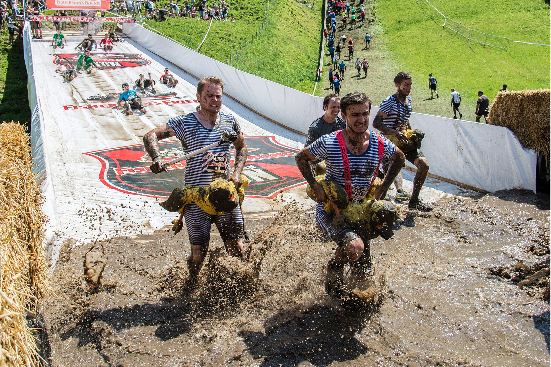 Bedruckte PVC Plane als Rutschbahn bei einem Mud Run mit weißen Seitenbannern und Teilnehmern im Schlammbecken