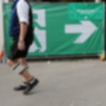 Notausgangsbanner rechts - als Fluchtwegkennzeichnung auf Volksfesten Notausgangsbanner mit Pfeil nach rechts am Bauzaun auf einem Festgelände, ein Mann in Tracht geht daran vorbei
