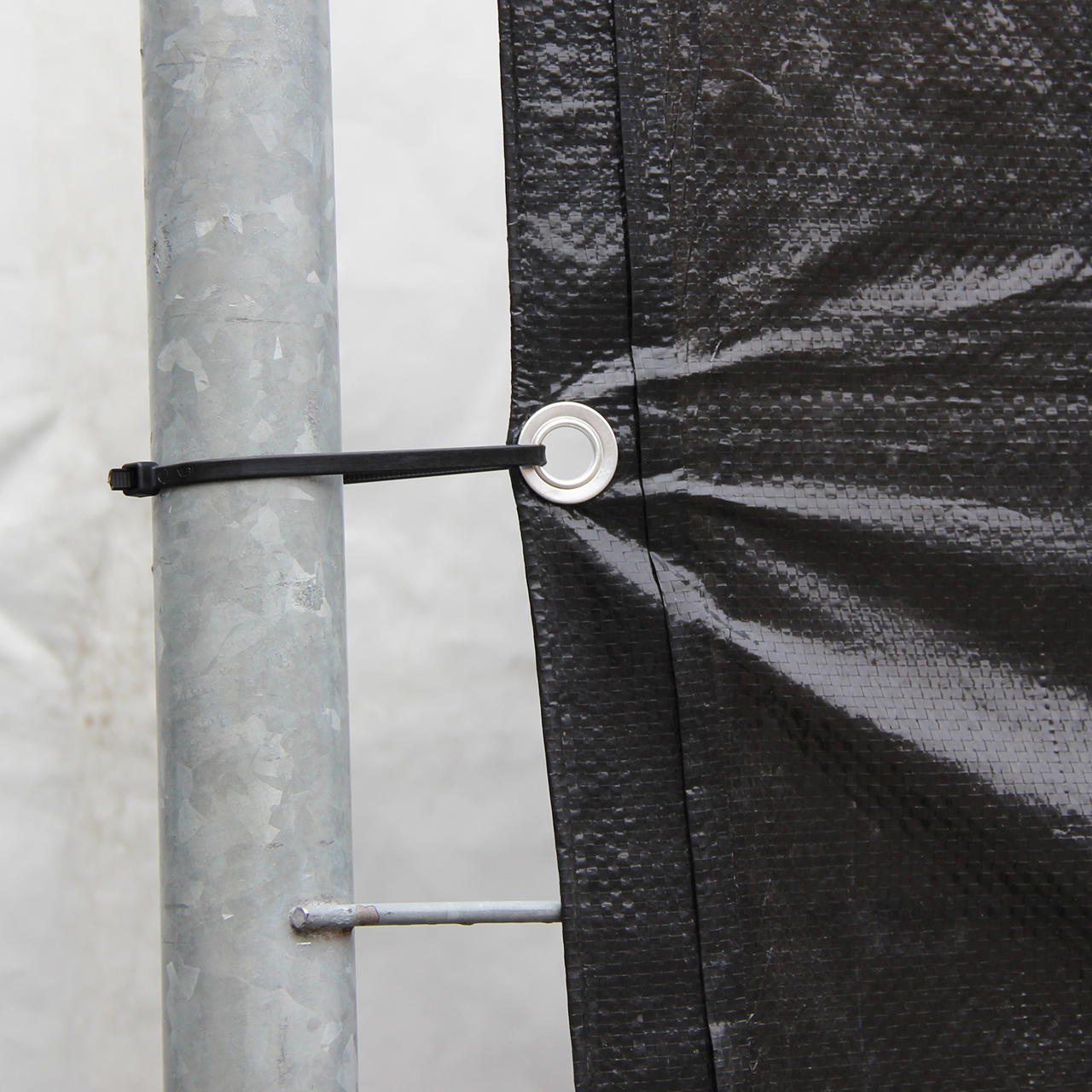 Nahaufnahme einer geösten, schwarzen Bauzaunplane, die mit einem schwarzen Kabebinder am Bauzaunrahmen befestigt ist