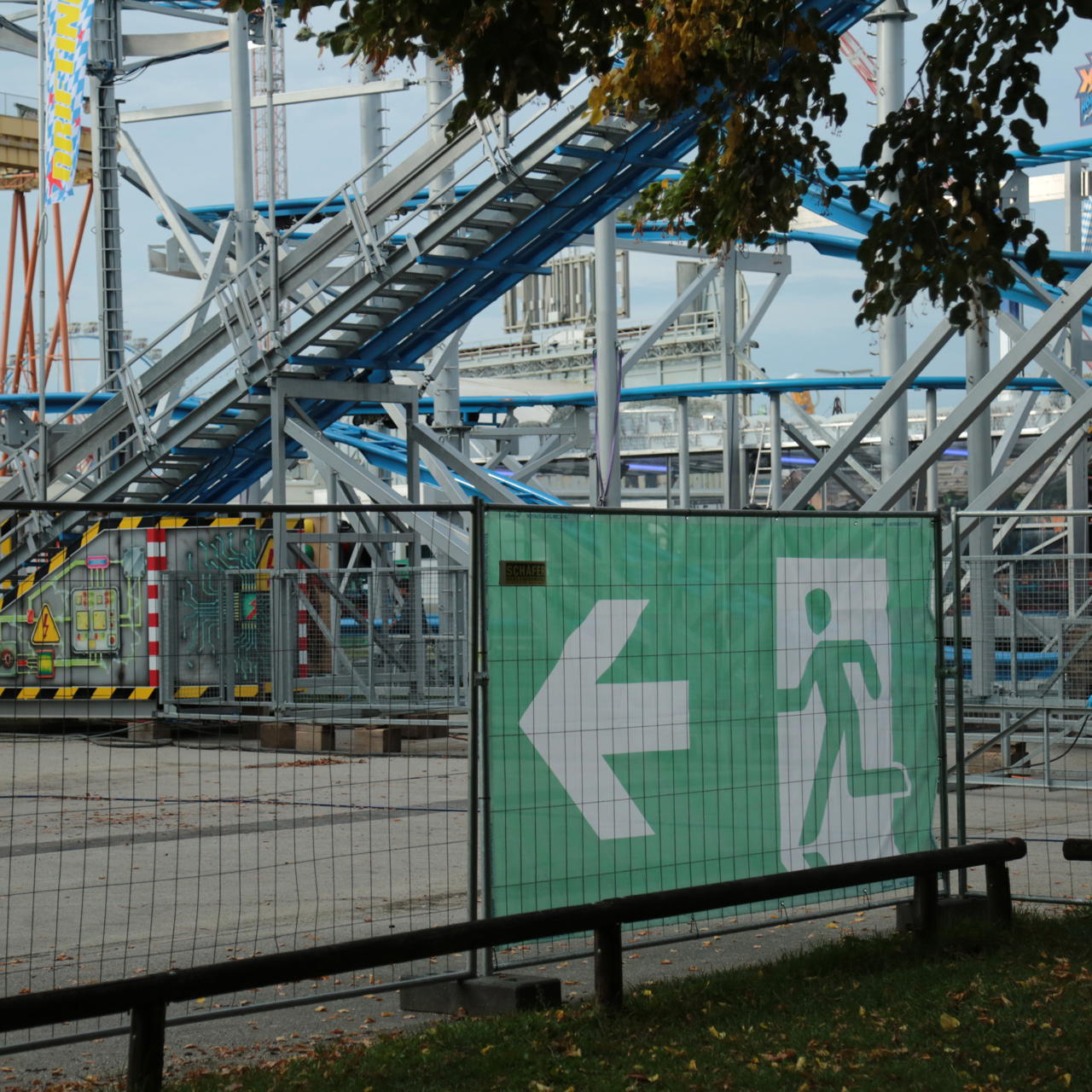Lichtdurchlässiges Mesh Banner mit Piktogramm Notausgang und Richtungspfeil, rückseitig am Bauzaun auf einem Volksfest