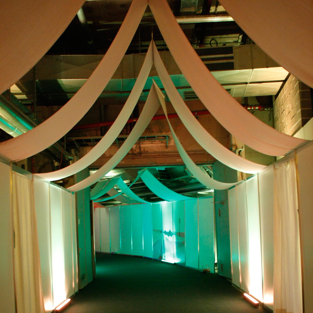 Dekorativ geschwungene Bahnen weißen Dekomoltons, gespannt über einen beleuchteten Gang mit seitlichen Trennwänden