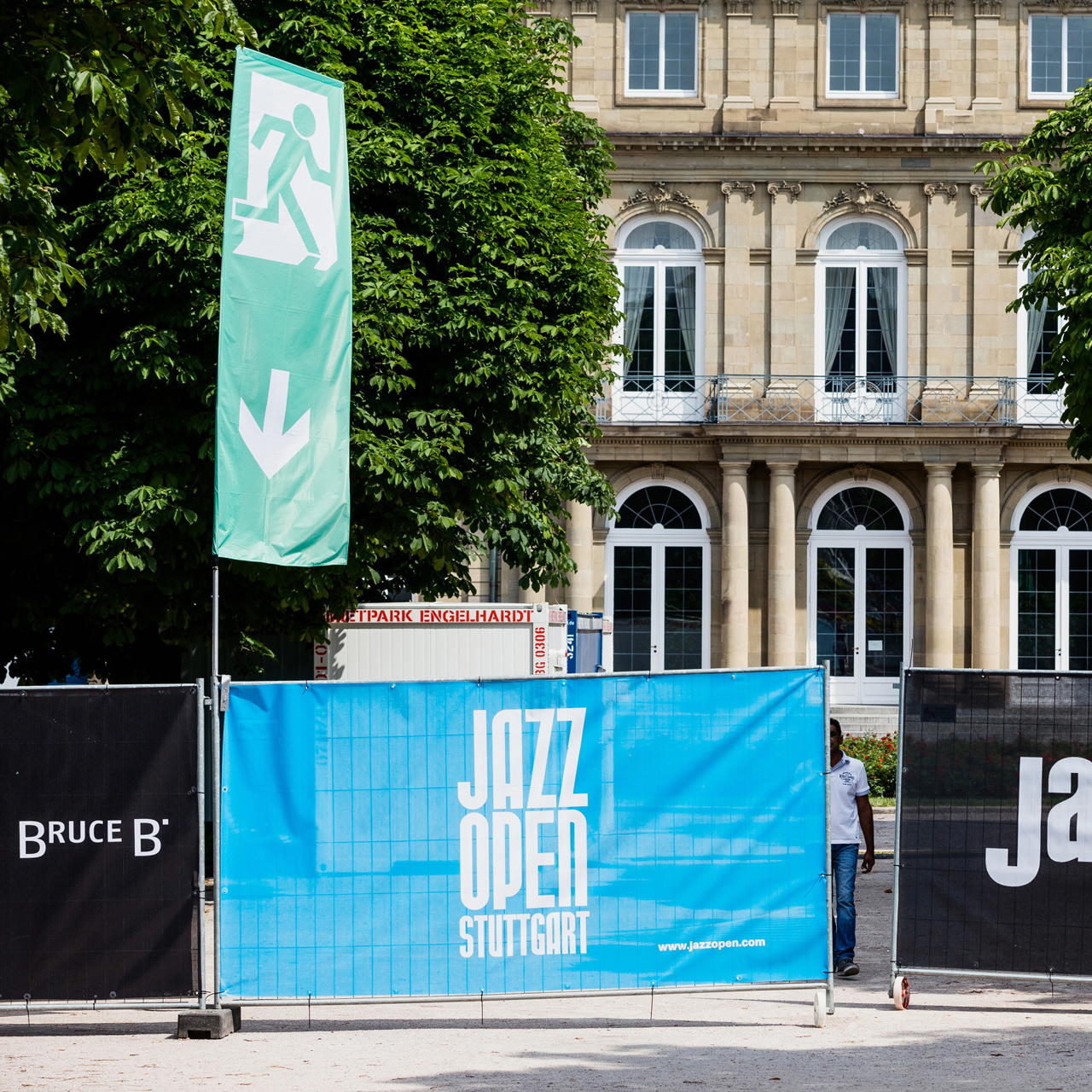 Bauzaunfahne mit Notausgangs-Piktogramm und Pfeil nach unten bei Jazz Open Stuttgart, montiert am Bauzaun