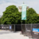 Bauzaunfahne mit Piktogramm Notausgang B1 - zertifiziert nach DIN 4102 Grüne Flagge mit weißem Notausgangs-Piktogramm und Pfeil nach unten an  einem Mobilzaun mit bedruckten Bauzaunplanen