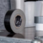 Gewebeklebeband schwarz - professionelle Verklebung für Events Schwarze Rolle Gewebeklebeband aufrecht auf einem Flightcase, im Hintergrund weitere Klebebandrollen