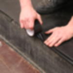 PVC Band GT 802 - abriebfeste Kantenverklebung für Bühnen und Stufen Detailaufnahme von abriebfestem, schwarzem PVC Tanzbodenband, das per Hand auf einer Bühnenkante angebracht wird