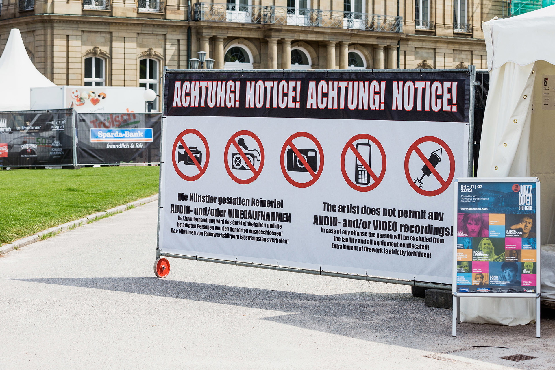 Geöstes Banner aus Netzvinyl mit Kabelbindern an Bauzaun befestigt mit Zugangshinweisen auf einem Open-Air-Event 