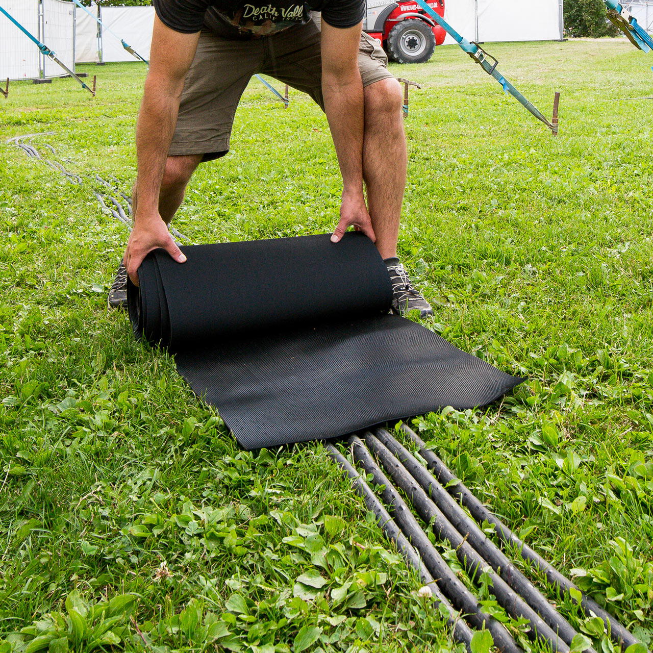 Kabelschutzmatte beim Ausrollen auf einer Wiese zur Abdeckung und zum Schutz von Kabeln auf einem Event 