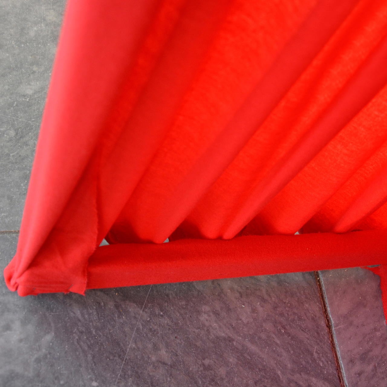 Detailaufnahme eines roten Dekomoltons in gleichmäßiger Faltung, unten gerafft und auf Steinboden gespannt