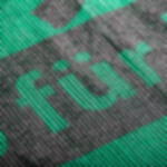 Tennisblende bedruckt als Werbeträger auf Sport- und Tennisplätzen Bildfüllende Nahaufnahme der Materialstruktur einer grünen Tennisblende mit digitalem Solventdruck in schwarz