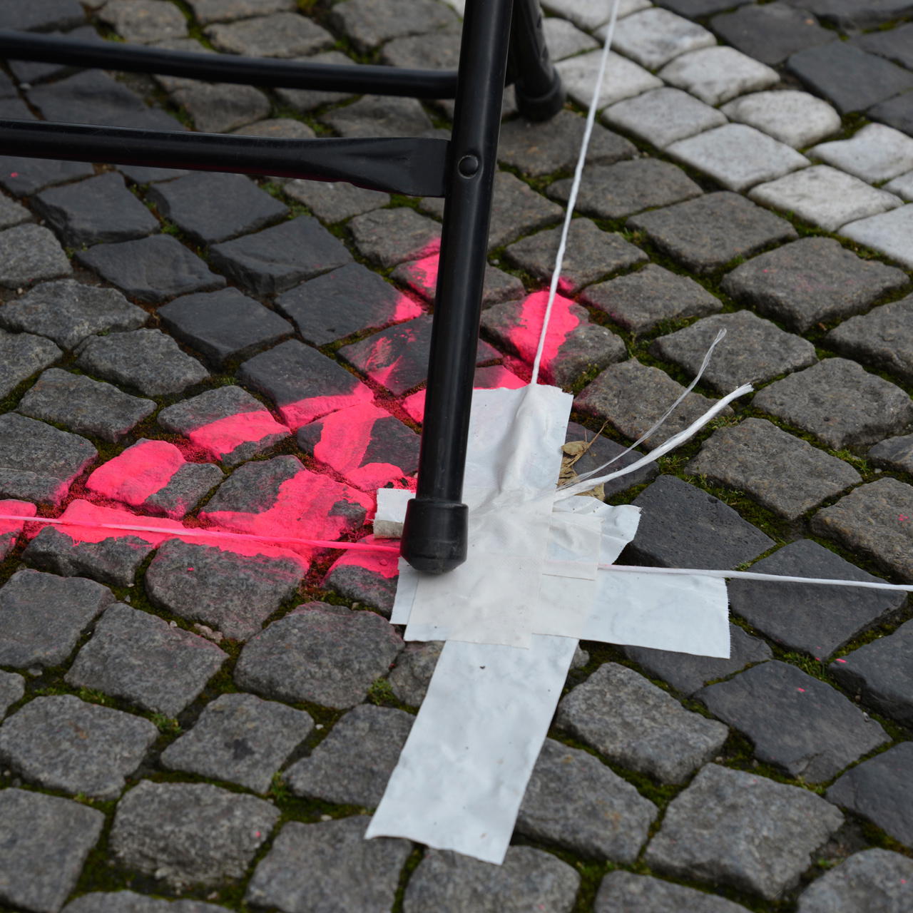 Weißes Gewebeklebeband verklebt auf unebenem Kopfsteinpflaster und über Fugen mit pinker Bodenmarkierung