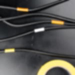 PVC Band GT 802 - formanpassungsfähiges Klebeband für Veranstaltungen  Schwarze Kabel mit farbiger Markierung aus formanpassungsfähigem PVC-Band in Orange, Weiß und Gelb, auf schwarzem Boden