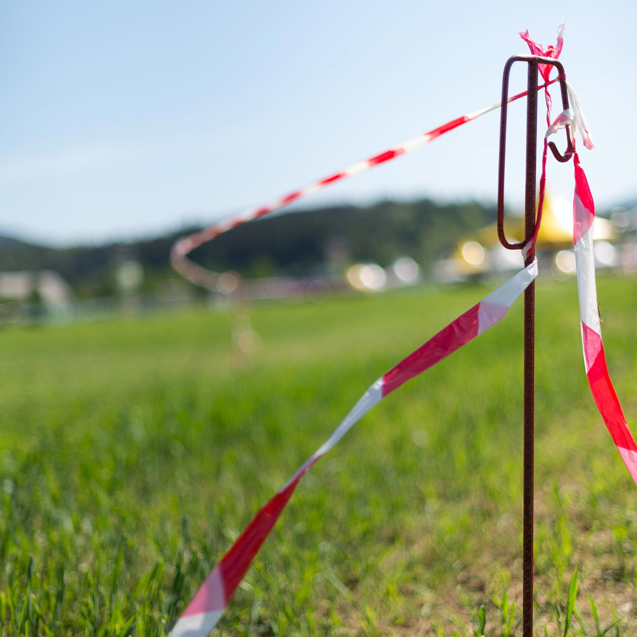 Rot-weißes Trassierband an einer Absperrstange befestigt zur Kennzeichnung eines Veranstaltungsbereichs auf einer WIese