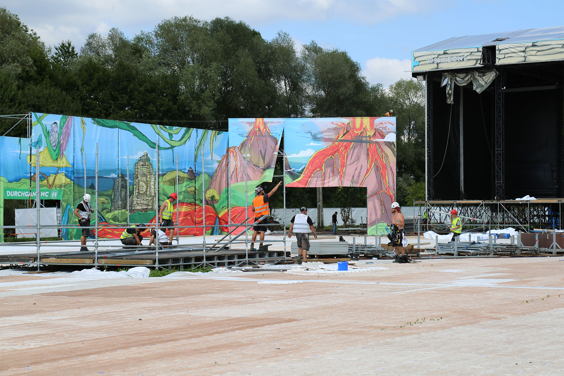 Künstlerisch bedruckte Frontlit PVC Banner mit Landschaftsmotiv beim Befestigen an Gerüstkonstruktion auf Festival