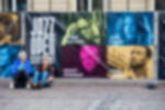Meshbanner - Werbebanner gesäumt und mit Ösen Bauzaun mit bedrucktem Mesh-Banner mit Künstlerporträts und Jazz Open Stuttgart Logo, davor zwei sitzende Personen
