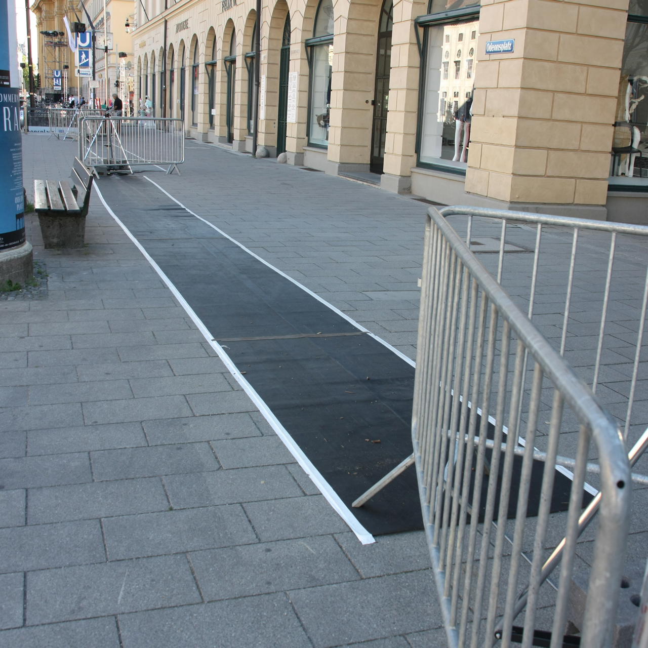 Temporär verlegter Gummiläufer auf städtischem Pflasterweg, beidseitig mit weißem Tape als Stolperschutz fixiert 