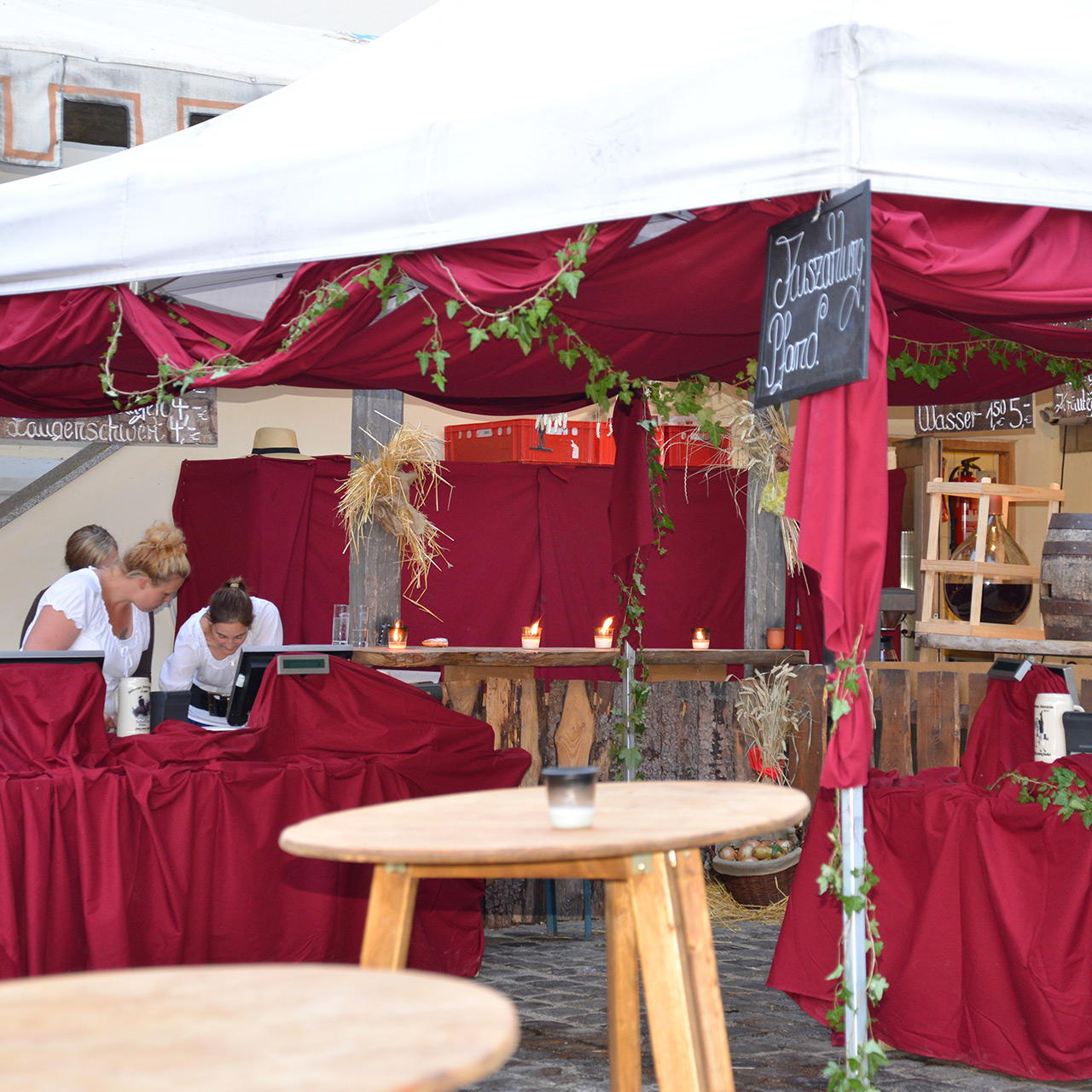 Rustikale Bar im Außenbereich unter weißem Pavillon mit bordeauxrotem Dekostoff als Barverkleidung und Dachauskleidung