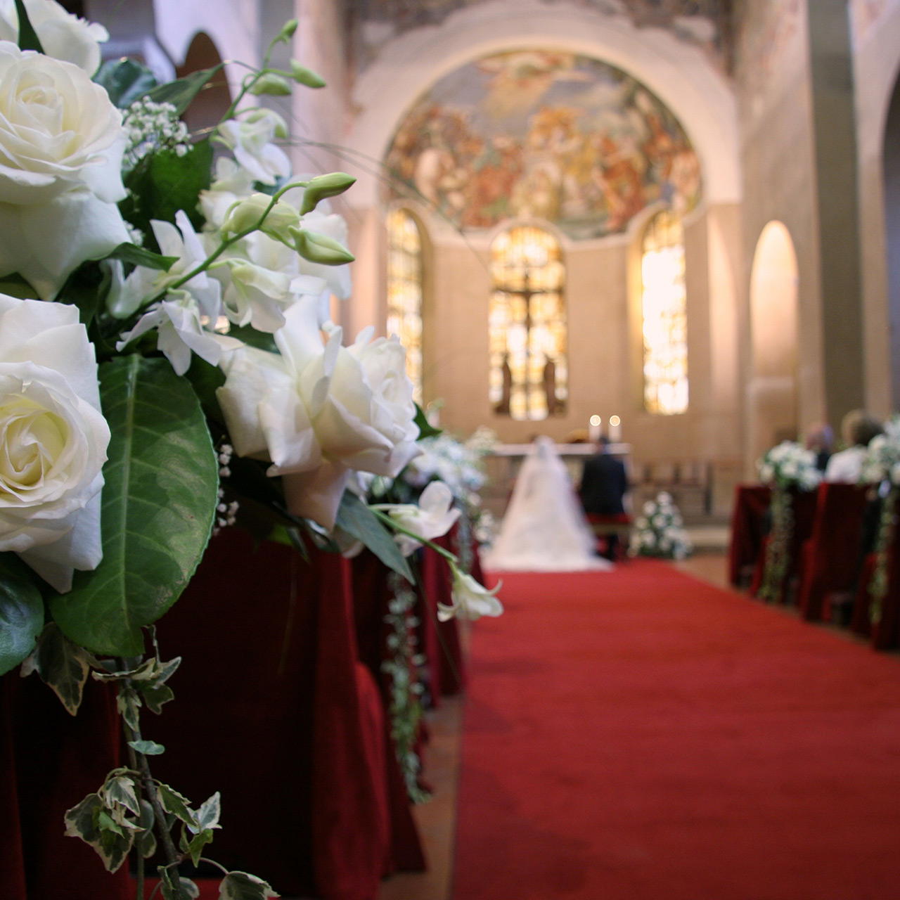 Blumenarrangements entlang eines roten Messeteppichs bei einer Hochzeit in der Kirche