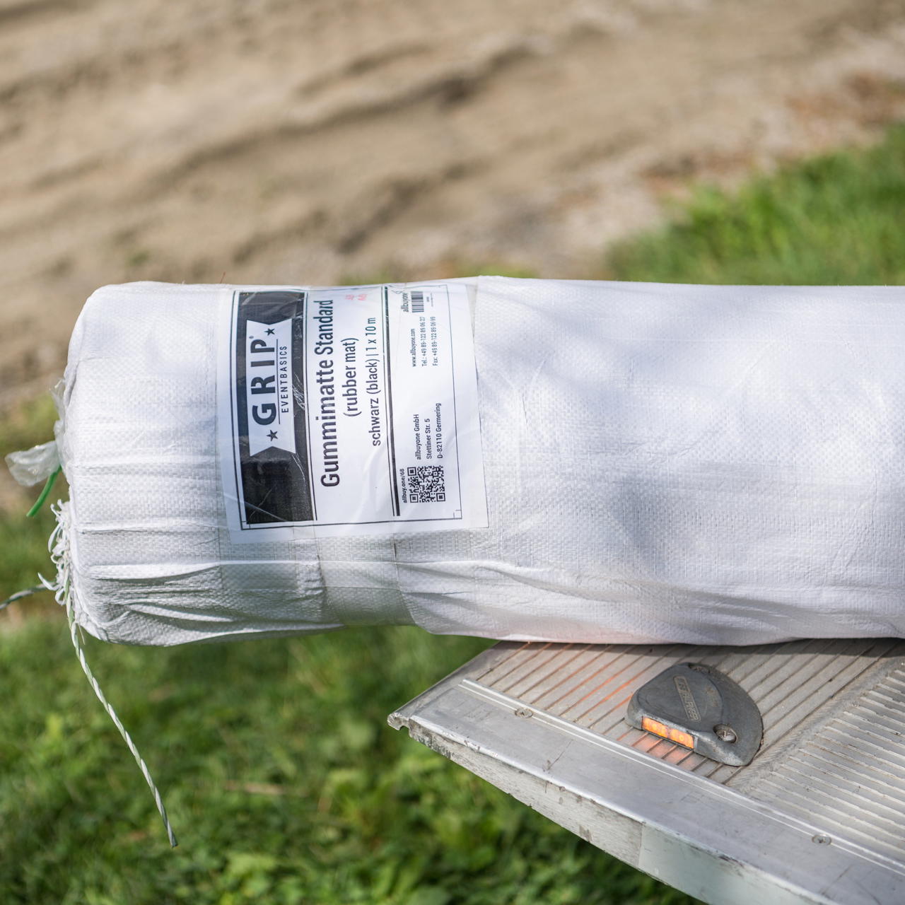 Nahaufnahme einer weiß verpackten Rolle Gummimatte mit Etikett liegend auf der Kante einer LKW Laderampe