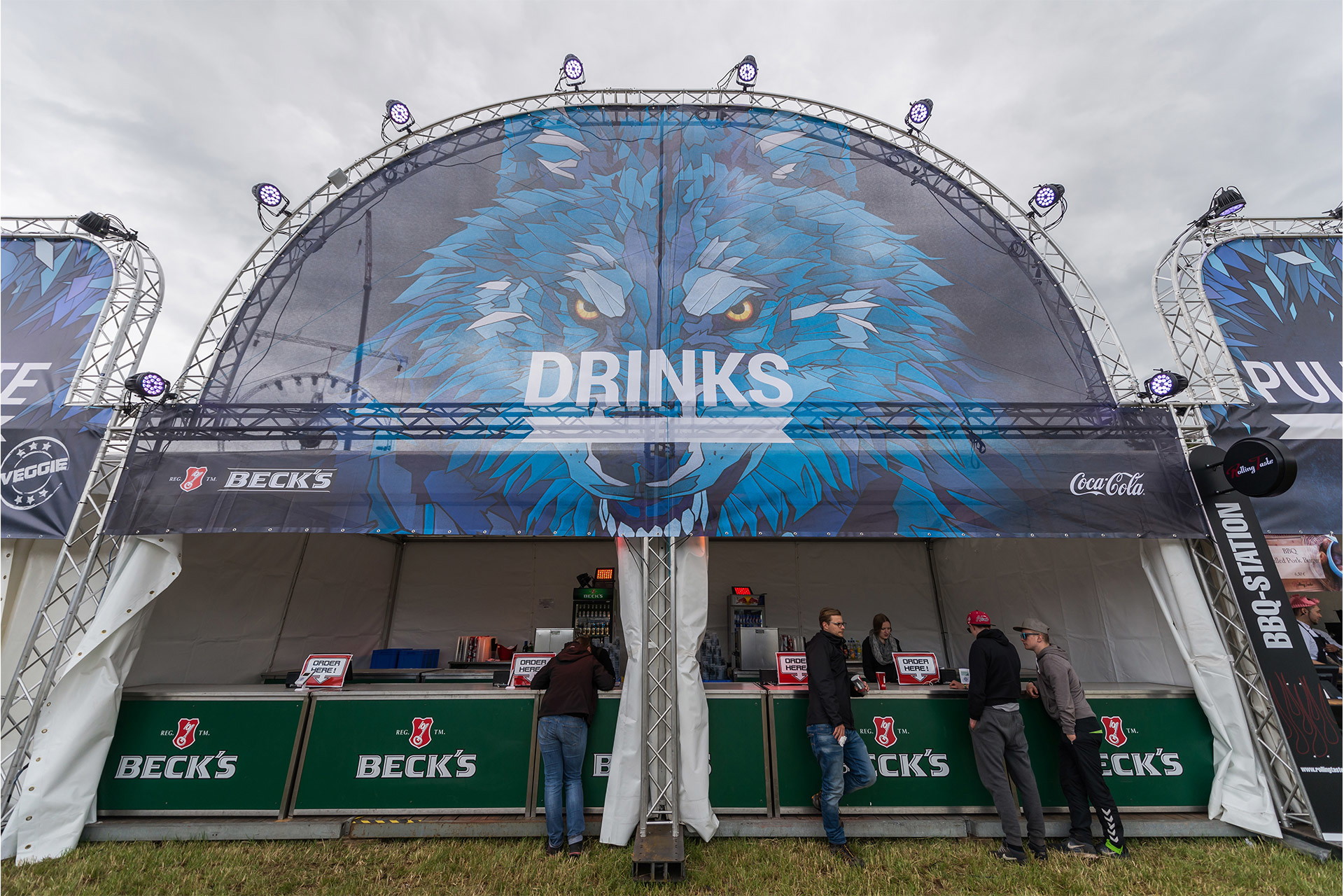 Festivalbar mit bedrucktem, halbrundem Gastrobanner über der Theke, Motiv eines blauen Wolfs und Schriftzug "Drinks"