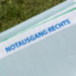 Notausgangsbanner rechts - Bauzaunbanner mit Sicherheitskennzeichnung  Nahaufnahme der Rückseite eines im Gras liegenden Meshbanners mit Aufdruck „Notausgang rechts“ im weißen Saum