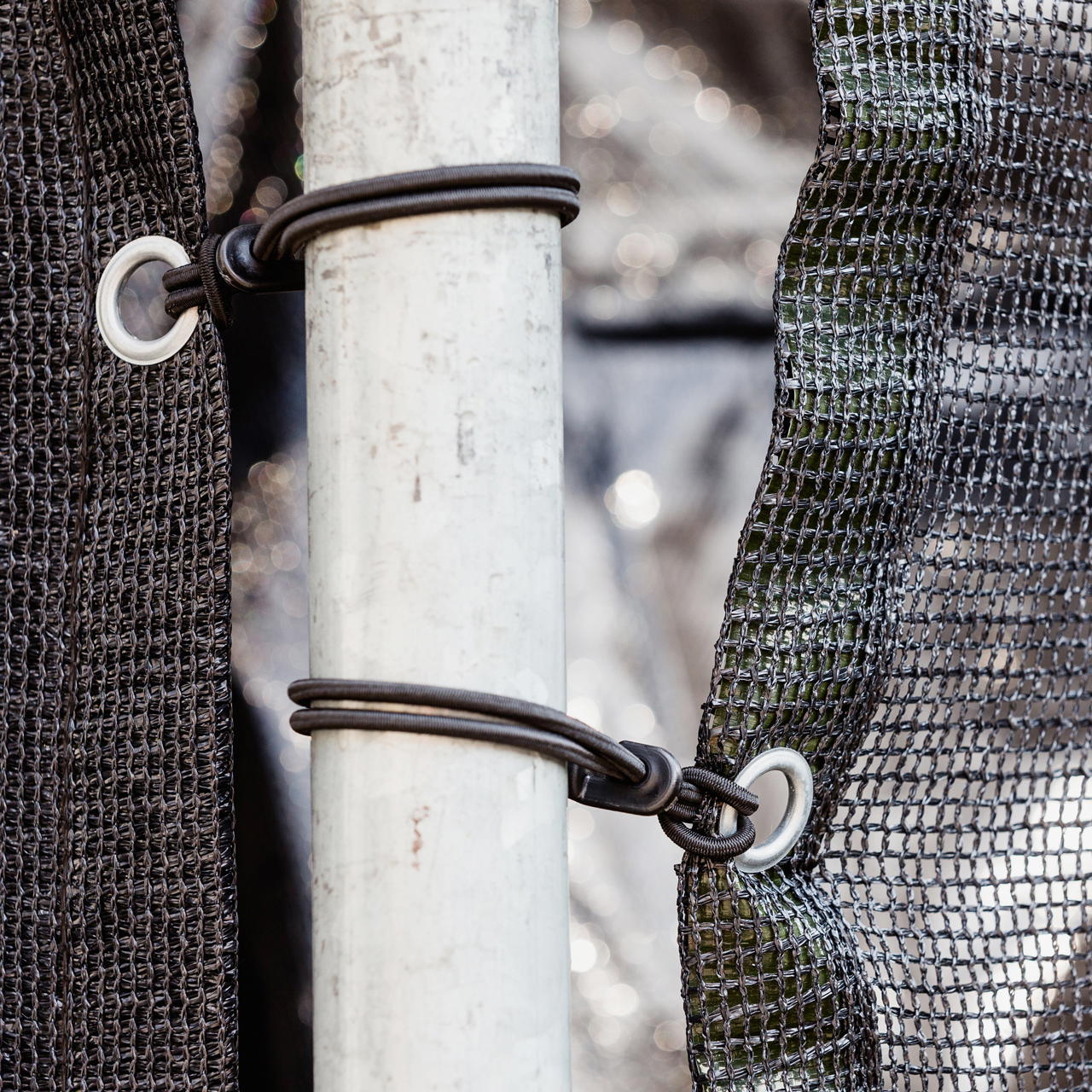 Nahaufnahme zweier geöster Netzgewebe-Planen, befestigt mit Gummispannern mit Haken an Gerüstrohr bei einem Event