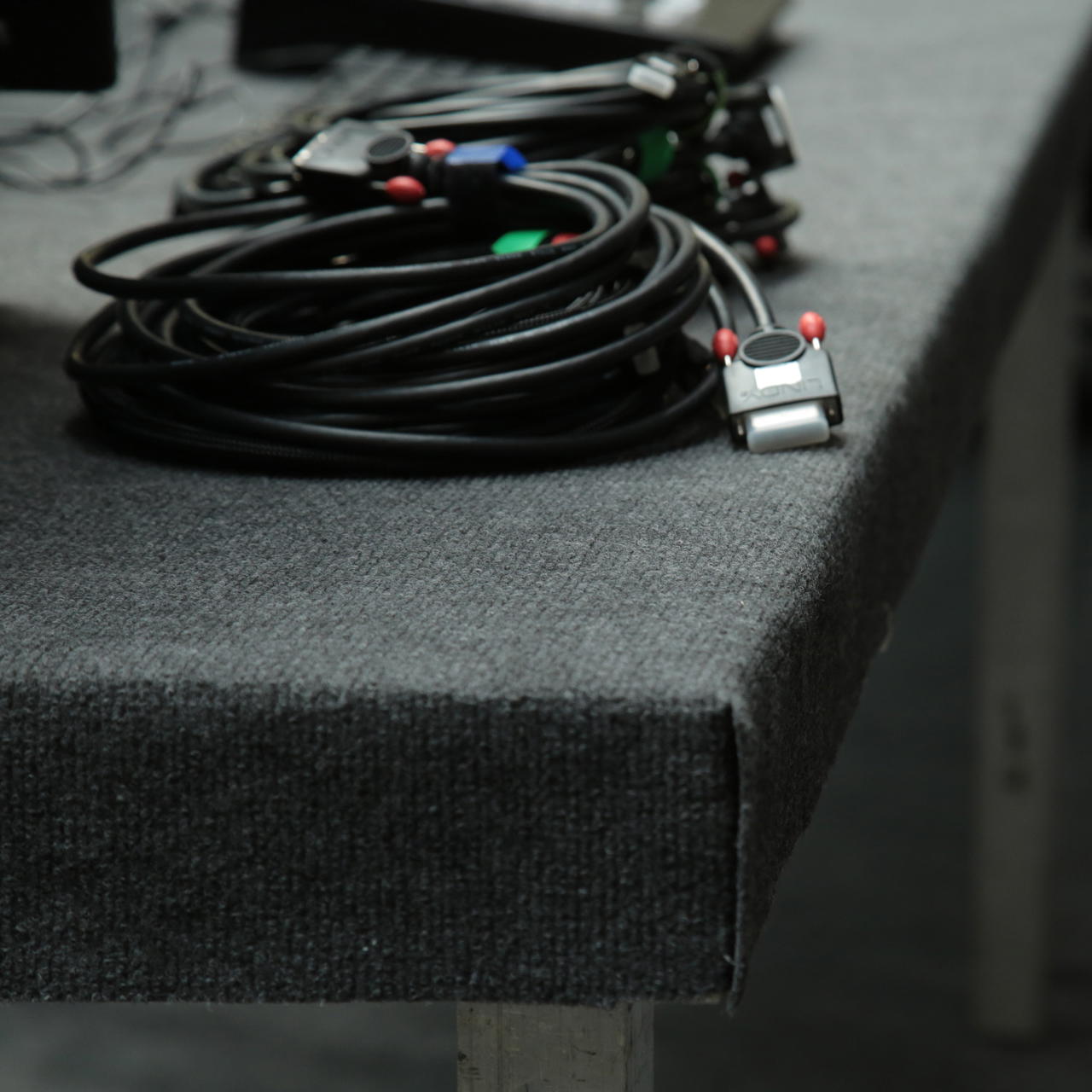 Grauer Messeteppich als Schutzunterlage auf einer Tischplatte, darauf liegen zusammengerollte Kabel