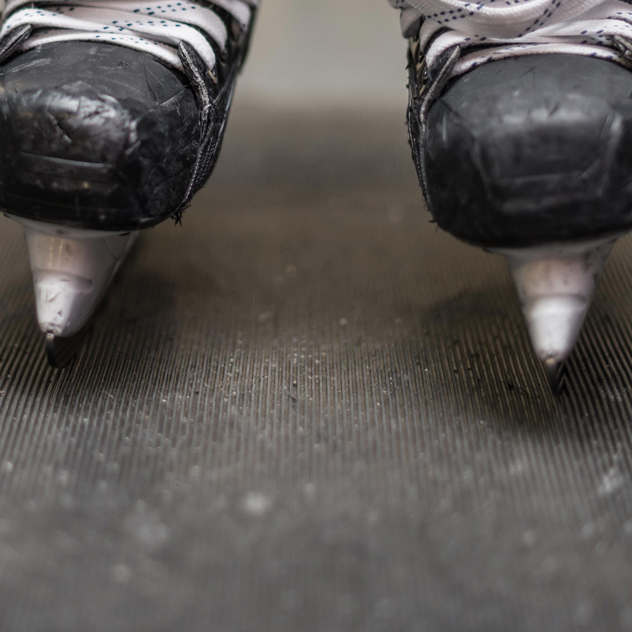 Ein Paar Eishockey-Schlittschuhe auf einem Gummiläufer mit Rippenstrucktur in Längsrichtung stehend 