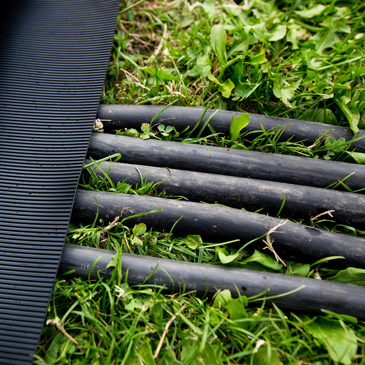 Nahaufnahme eines Gummiläufers als temporärerer Kabelschutz auf einer Wiese, darunter liegen mehrere Kabel