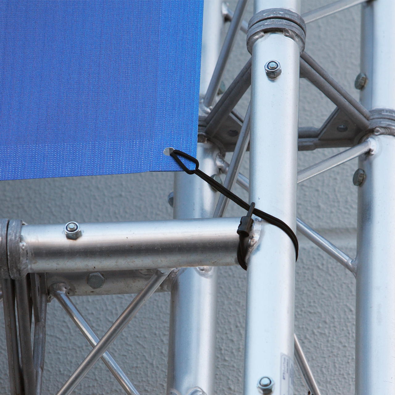 Spannfix mit Haken befestigt eine geöste blaue Plane an einer Traversenkonstruktion im Außenbereich bei einem Event