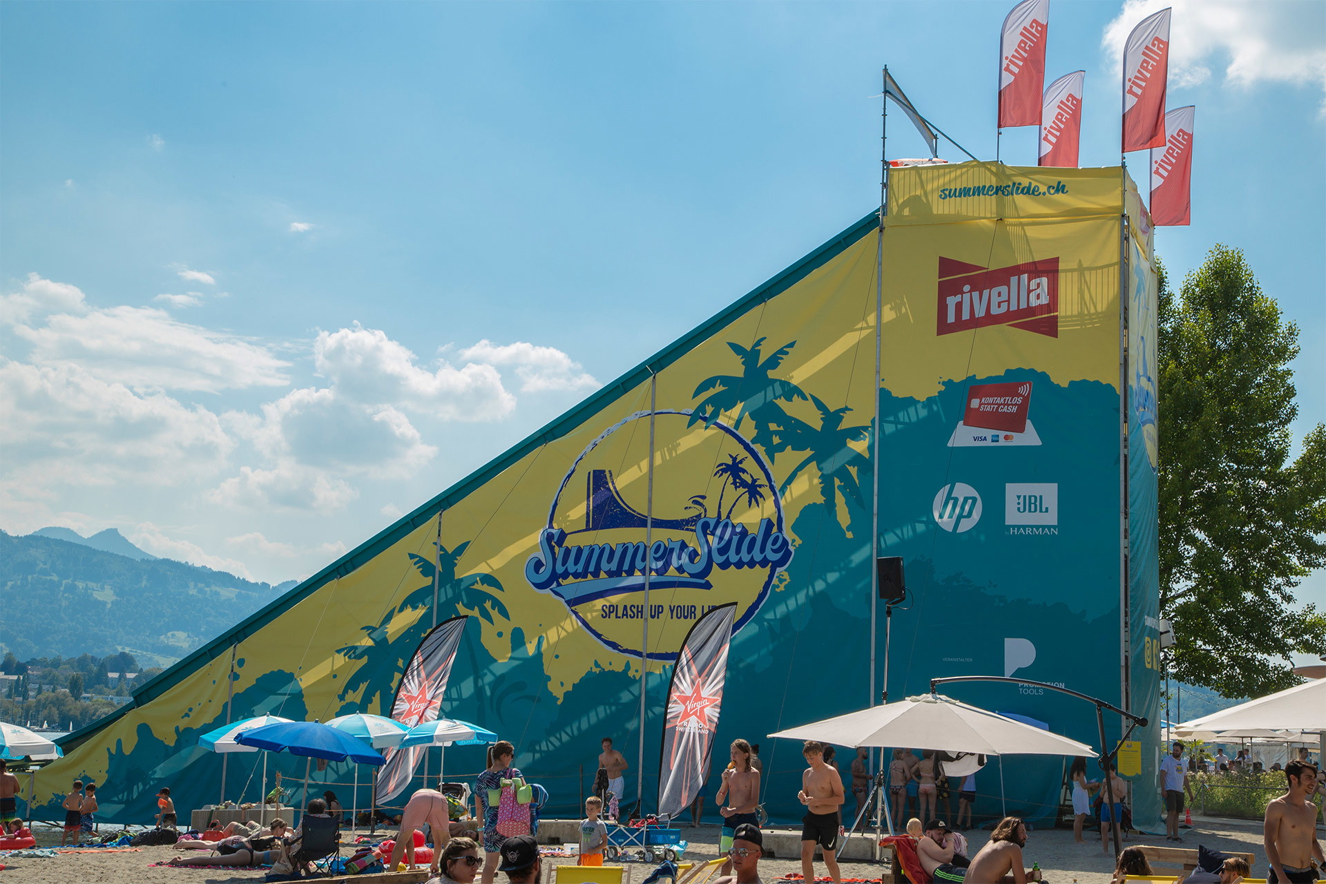 Großflächig bedruckte PVC Plane mit Sommermotiv und Sponsorenlogos auf geneigter mobiler Wasserrutsche mit Badegästen