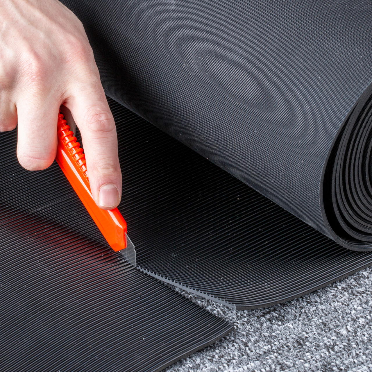 Nahaufnahme eines schwarzen Gummiläufers, der auf dem Boden liegend mit Cuttermesser zugeschnitten wird