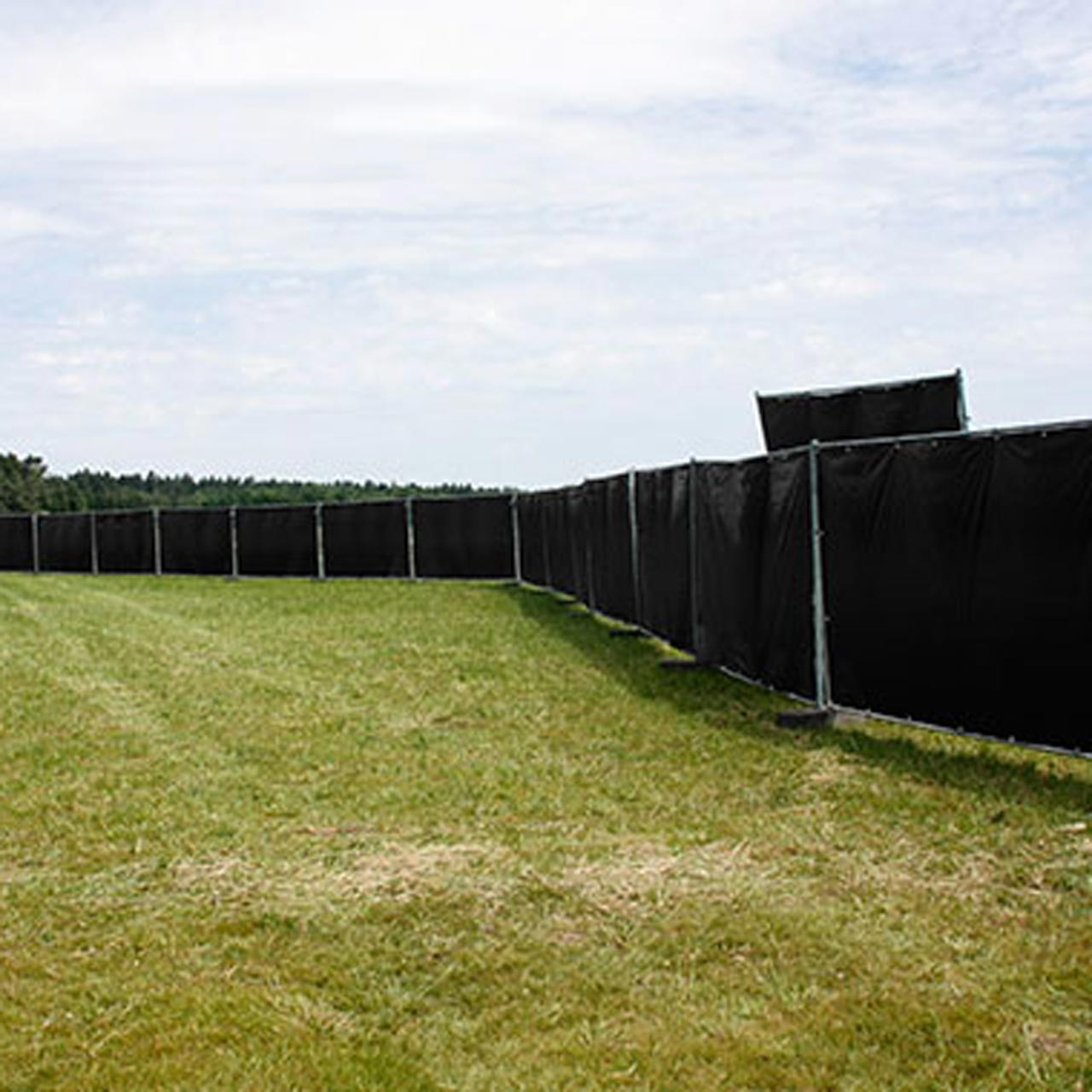 Schwarze Gewebeplane als Sichtschutz an langer Bauzaunreihe auf einer Wiese 