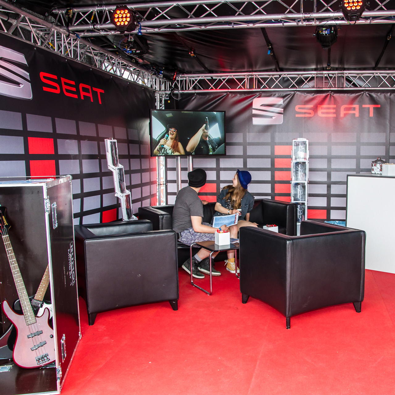 Roter Eventteppich verlegt in einem Präsentationsstand mit schwarzen Sitzmöbeln, Monitor und gebrandetem Rückwandsystem