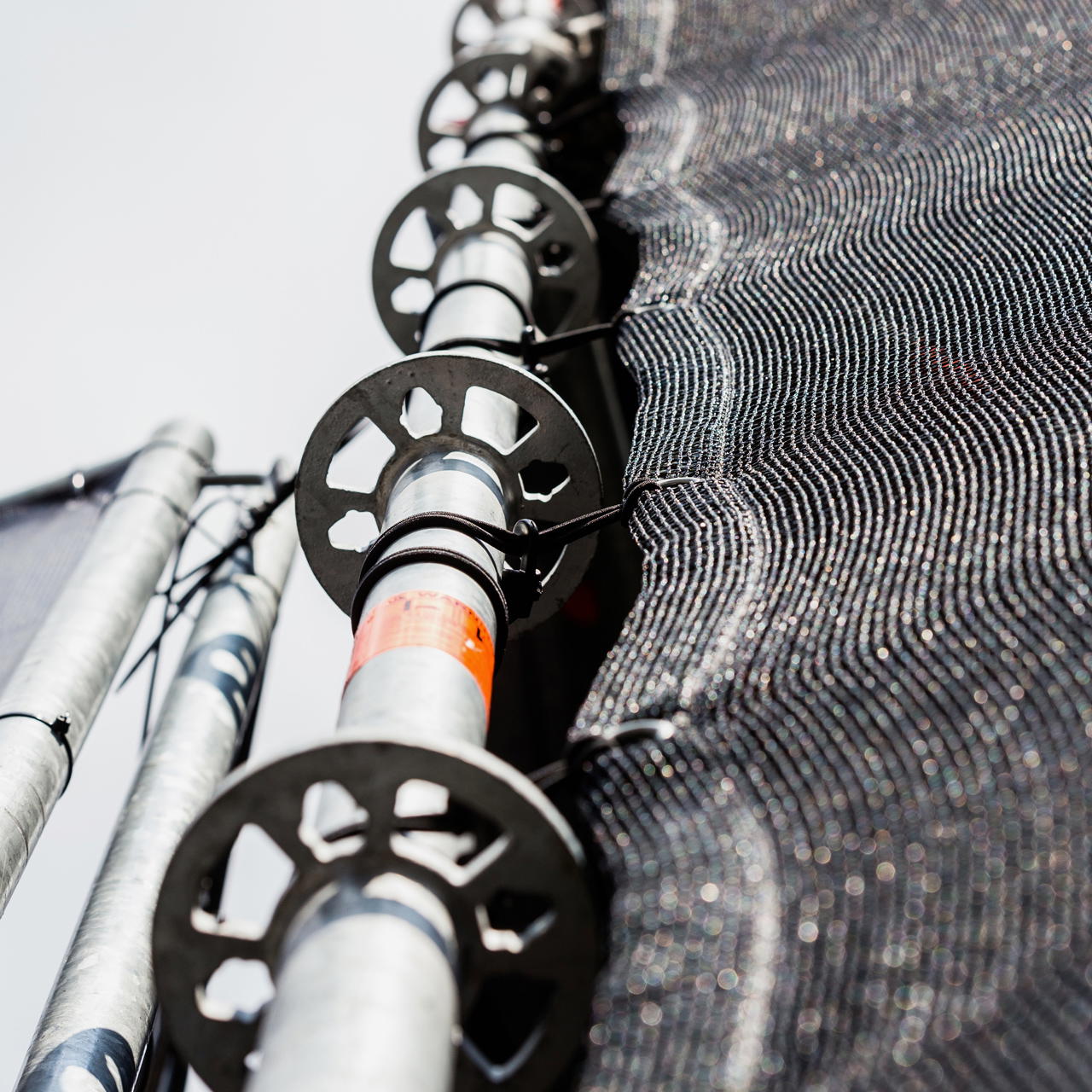 Nahaufnahme der Befestigung eines geösten Banner-Netzgewebes mit Spannfixen an einem Gerüstgestänge bei einem Event