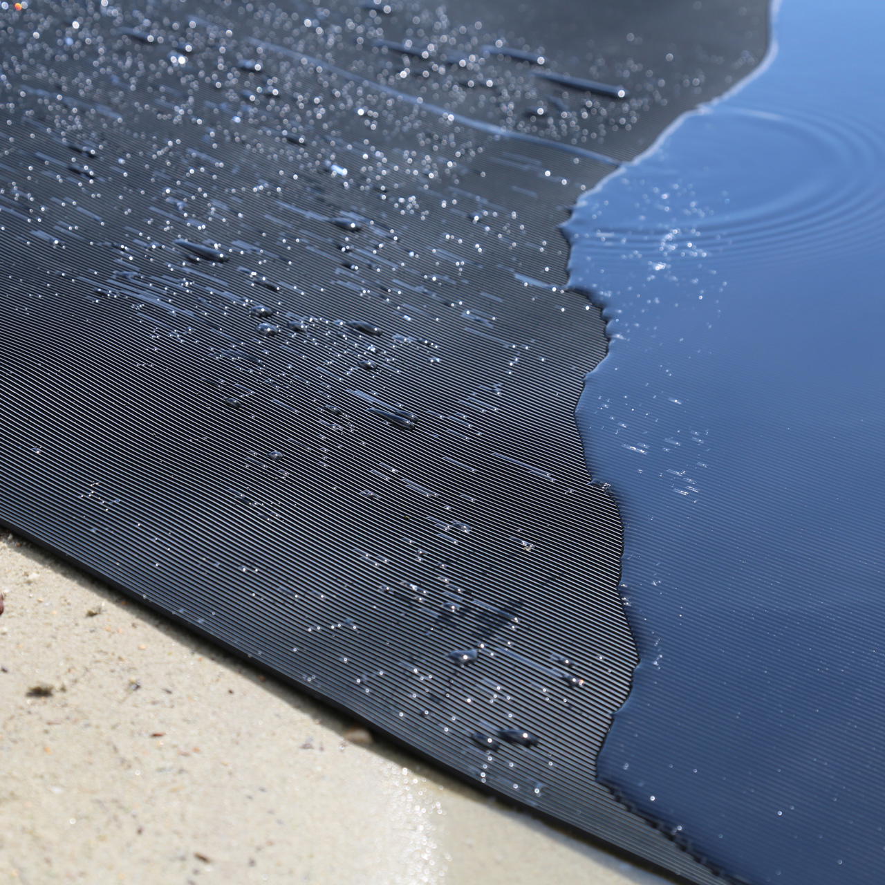 Nahaufnahme einer schwarzen Kabelschutzmatte mit Wasserperlen und Regenpfütze darauf