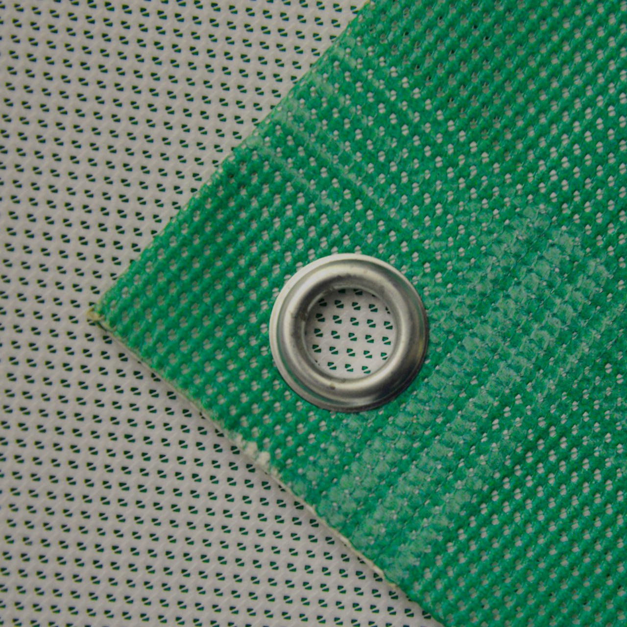 Detailaufnahme der Ecke eines grünen Mesh-Banners mit PVC Beschichtung, randverstärkt und mit Öse zur Befestigung 